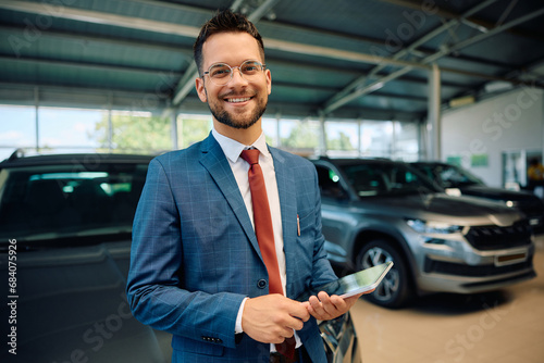 Happy salesman with touchpad at car dealership looking at camera. © Drazen