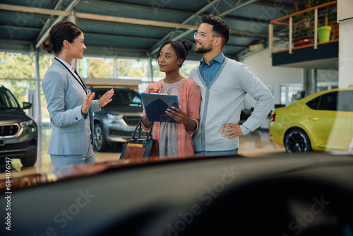 Young couple talks to car saleswoman while buying new car in showroom.