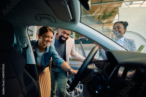 Happy multiracial couple looking at new car in showroom.