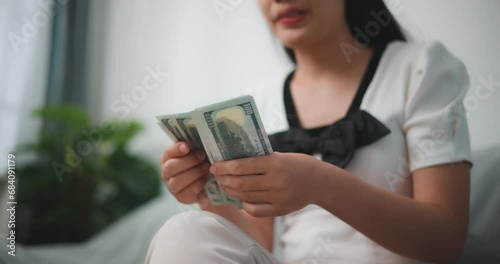 Footage of Happy young asian woman counts cash dollar bills while sitting in living room at home,counting stack cash money dollar photo