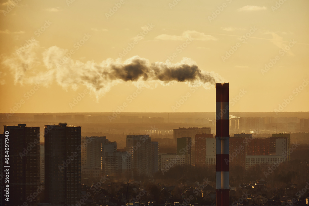 Smoke from a tall chimney over a winter city with houses in the snow