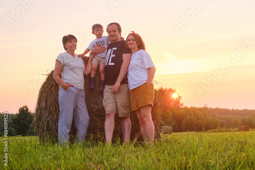 A happy family enjoys the summer evening as the father holds her baby boy in her arms, surrounded by stacks of straw in a picturesque field.