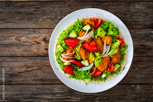 Seared chicken nuggets with vegetable salad on tortilla on wooden background 