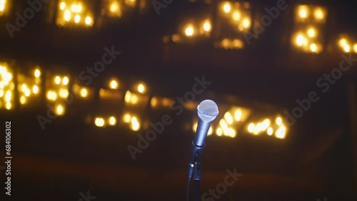 Single microphone on empty stage in large vintage concert hall with ceiling glowing with warm light. Event kickoff intrigue anticipation concept, low angle shot