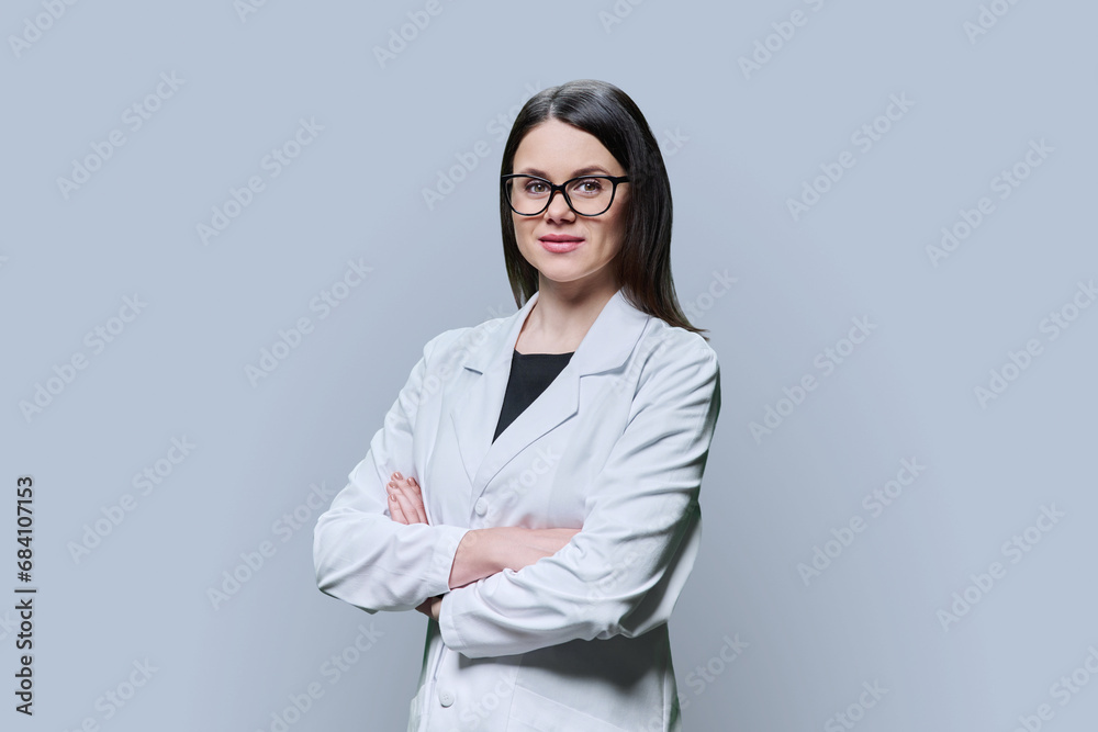 Woman medical scientist, pharmacist in white coat with crossed arms on grey background Woman medical scientist, pharmacist in white coat with crossed arms on grey background