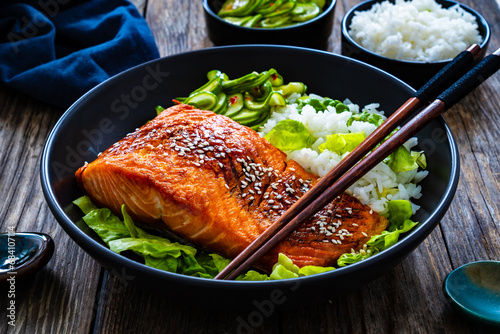 Fried teriyaki salmon steak with white rice and sliced cucumber on wooden table 