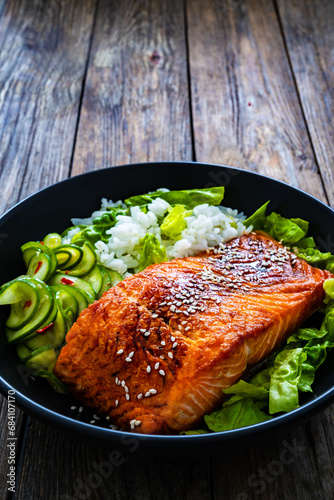 Fried teriyaki salmon steak with white rice and sliced cucumber on wooden table

