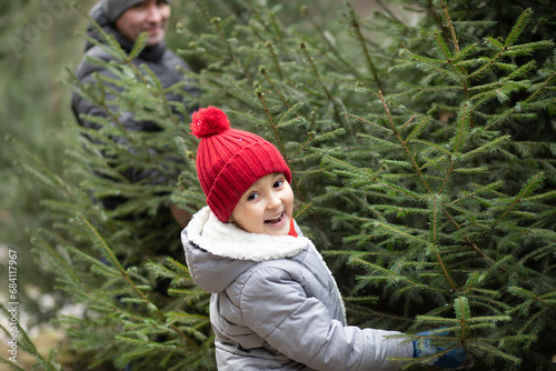 Cute little kid choosing with family freshly cut Christmas tree at outdoor fair. Holiday celebration concept.
