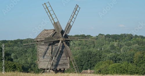 Old windmill stands in field, green trees, forest. Pirogovo Museum, Kiev, Ukraine. photo