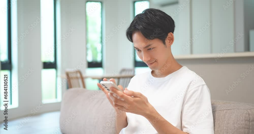 ソファに座ってスマートフォンでゲームをする男性 ソファに座ってスマートフォンでゲームをする男性