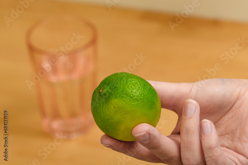 Zielona limonka trzymana w dłoni, w tle szklanka z wodą