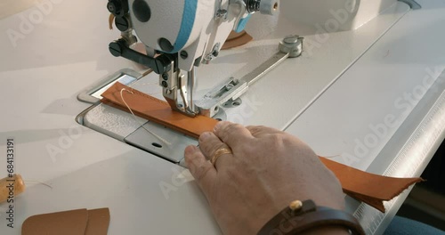 male craftsman stitches a men's leather belt on a sewing machine Close up shot slow motion photo