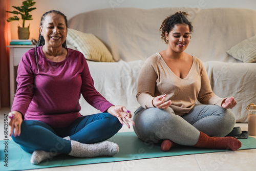 Happy african mother and adult daughter doing yoga meditiation at home during winter time photo