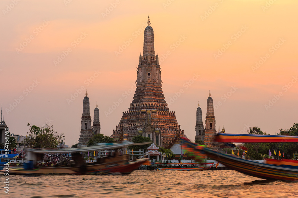 Obraz premium Wat Arun Ratchawararam Ratchawaramahawihan at sunset time The foreground is the Chao Phraya River. There are tour boats passing by. It is a recommended tourist attraction in Bangkok, Thailand.