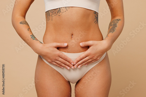 Close up cropped young nice lady woman with slim body perfect skin wear nude top bra lingerie stand put hands arms on belly isolated on plain pastel light beige background. Lifestyle diet fit concept. © ViDi Studio
