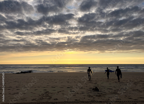 A group of surfers on their way to the Atlantic Ocean with the setting sun in front of them