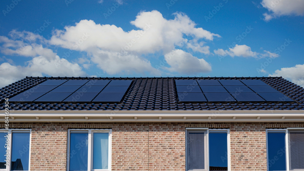 Fototapeta premium Newly built houses with black solar panels on the roof against a sunny sky Close up of new building with black solar panels. Zonnepanelen, Zonne energie, Translation: Solar panel, Sun Energy