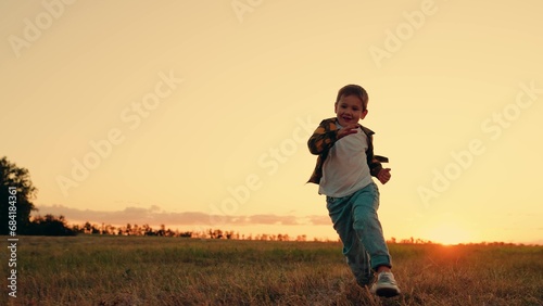 Dream kid Joyful little boy running at sunset. Kid is running across field. Child boy runs through green grass in sun. Childhood dream happiness concept. Happy child playing in nature. Happy family.