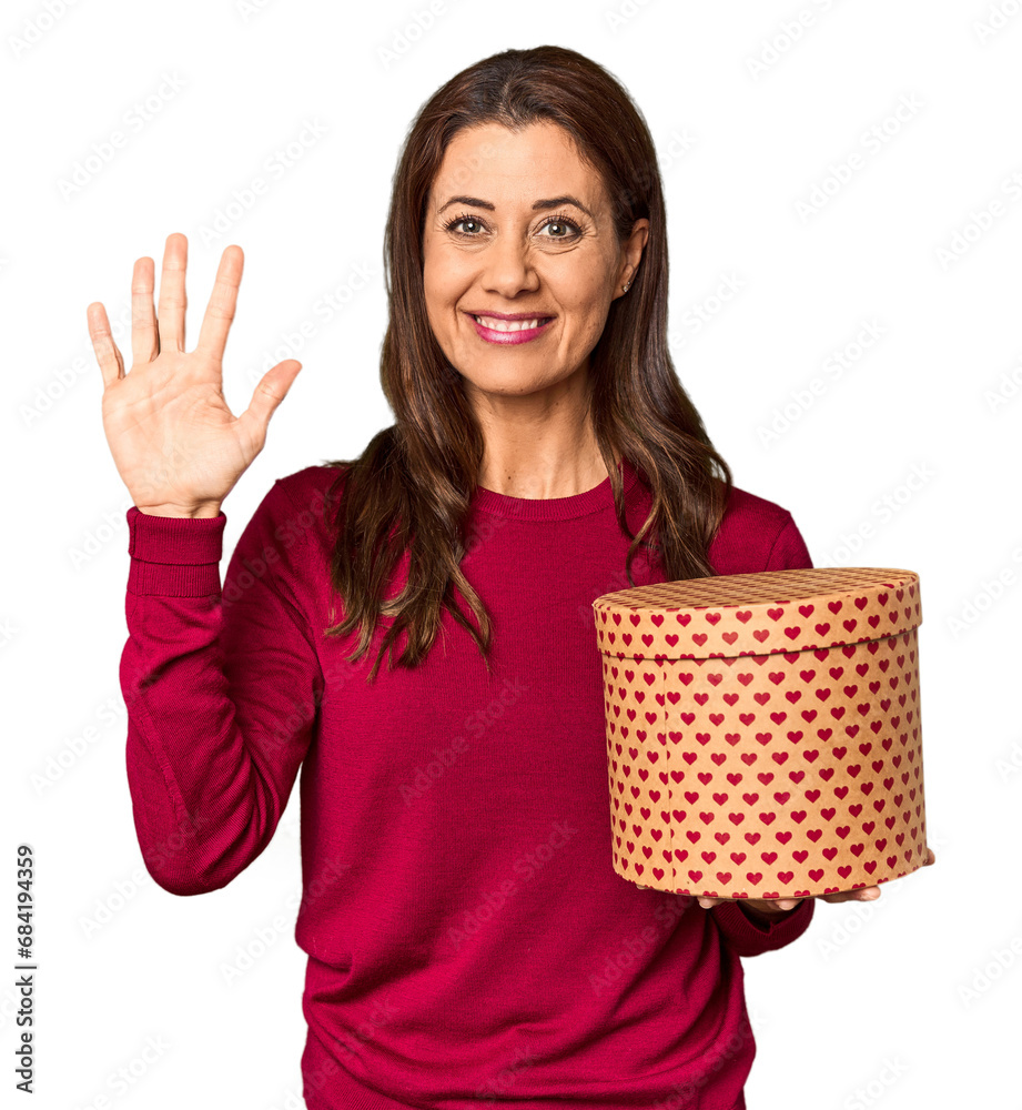 Middle-aged woman with Valentine's Day heart box in studio smiling cheerful showing number five with fingers.