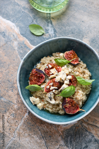 Green bowl with figs and blue cheese risotto, vertical shot on a beige and grey granite background, high angle view