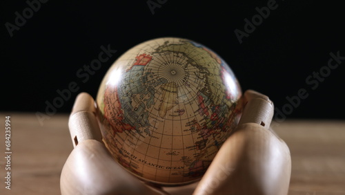 On a black background, a wooden model hand holds the Earth, symbolizing the importance of protecting the environment and loving the planet.