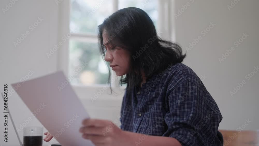 Midlife Asian woman working on her laptop in the living room at home on a leisure day Midlife Asian woman working on her laptop in the living room at home on a leisure day