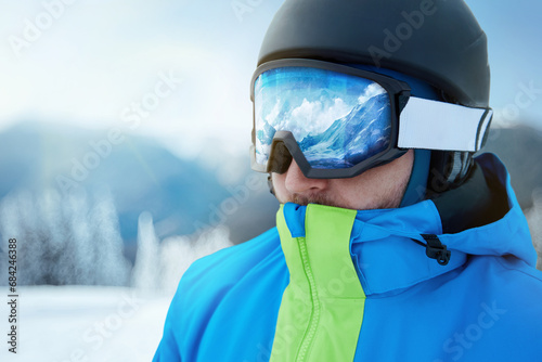 Close up of the ski goggles of a man with the reflection of snowed mountains. A mountain range reflected in the ski mask. Man on the background blue sky. Wearing ski glasses. Winter Sports.