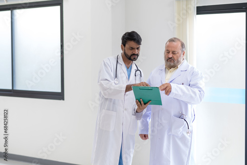 Concentrated mature and young male doctors in white medical uniforms look at clipboards and discuss patient anamnesis together. team brainstorming make decision concept.