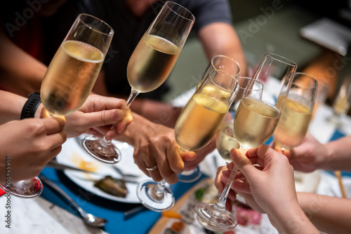 A group of people raise a toast with glasses of Prosecco or sparkling wine on the table © moomusician