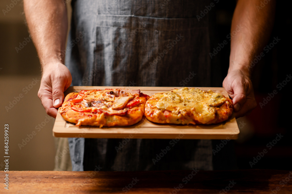 Rustic Pizza Moment: A snapshot of male hands showcasing two small homemade pizzas on a wooden board