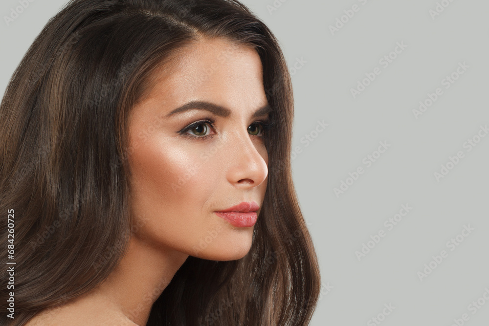 Pretty woman brunette with long dark healthy wavy hair and makeup on gray background. Beautiful face close up, studio portrait Pretty woman brunette with long dark healthy wavy hair and makeup on gray background. Beautiful face close up, studio portrait