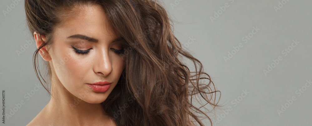 Naklejka premium Glamorous fashion model with dark healthy hairstyle, fresh clean skin and trendy make-up looking at camera on gray background. Brunette woman portrait