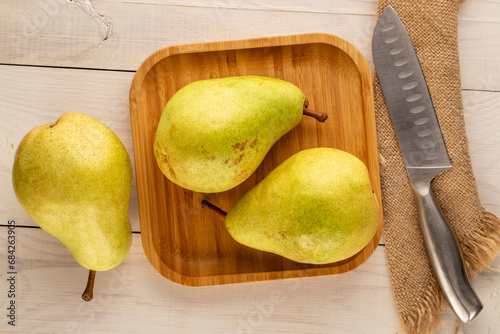 Three organic ripe pears with bamboo plate and knife on wooden table, macro, top view.