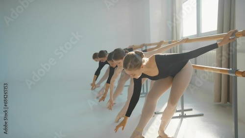 Group of young women dance ballet in dance class. Dancing ballerinas gracefully raise their hand during training