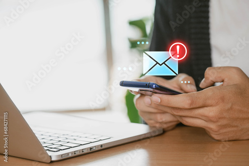 A businessman at home using a smartphone to receive email warning alerts about spam, hackers, junk and trash mail, virus, and network security concepts