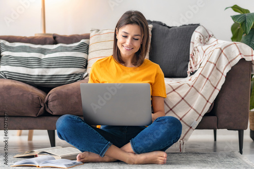 Online education distance learning concept. Happy young caucasian woman study in front of the laptop computer at home sitting on the floor near the sofa