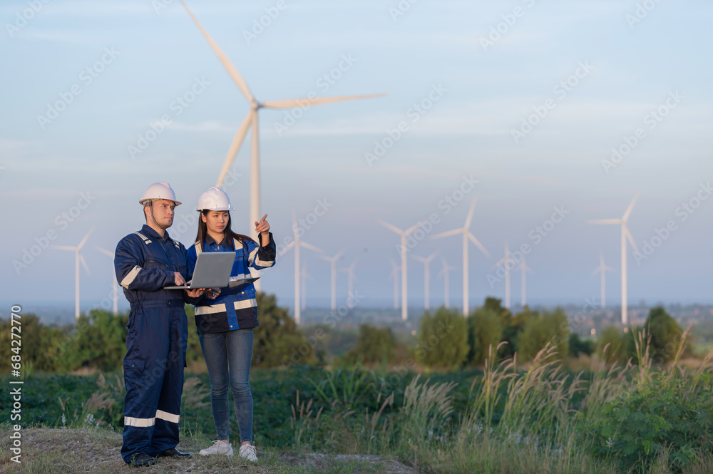 Two engineers working and holding the report at wind turbine farm Power Generator Station on mountain,Thailand people,Technician man and woman discuss about work Two engineers working and holding the report at wind turbine farm Power Generator Station on mountain,Thailand people,Technician man and woman discuss about work