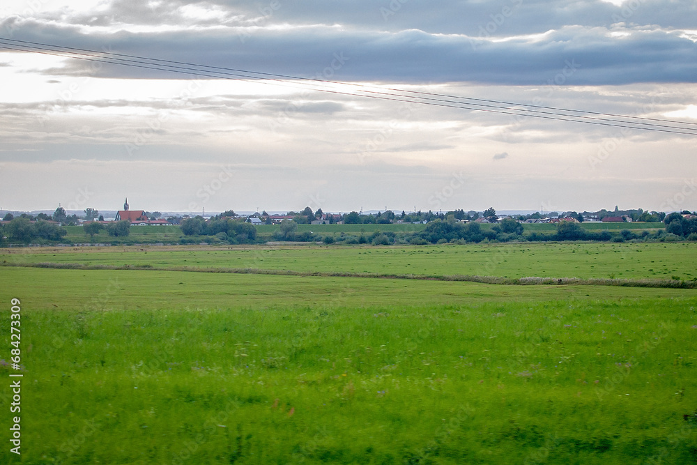 Green farm meadows and a European village in the distance on the horizon. European rural landscape in the evening