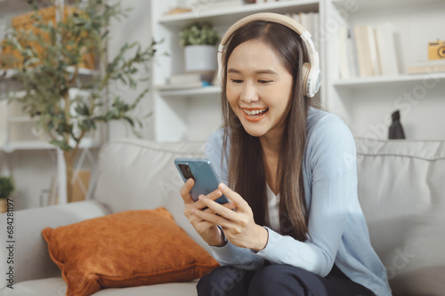 Happy asian woman listening to music from mobile phone while sitting on the the sofa at homes, Smiling girl relaxing with headphones in morning, Time to relax. copy space. #684281197