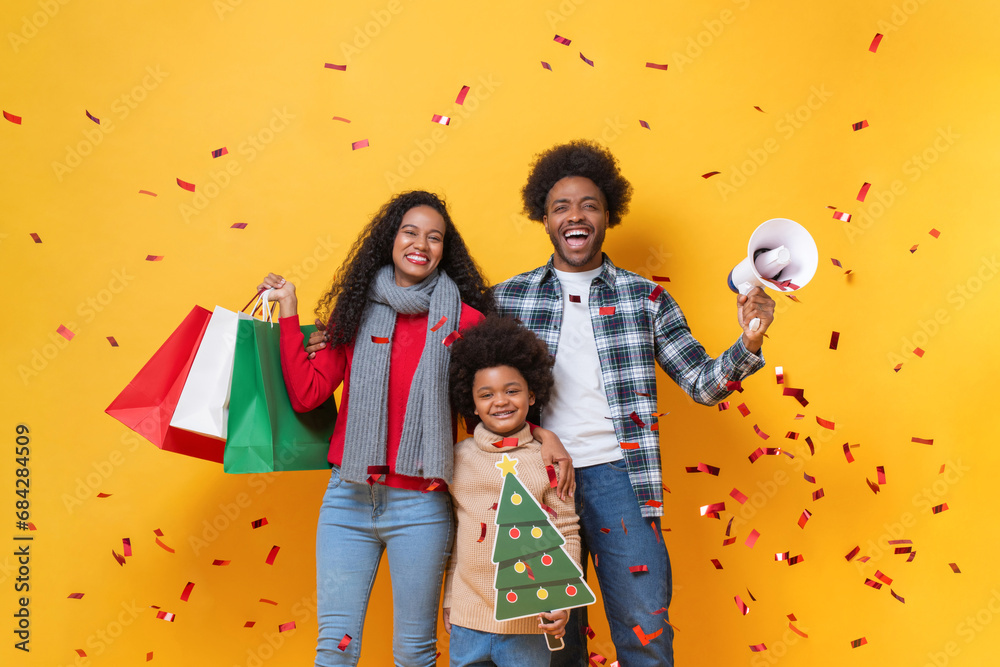 Happy African American family in festive Christmas celebration studio shot yellow color background with confetti - obrazy, fototapety, plakaty 