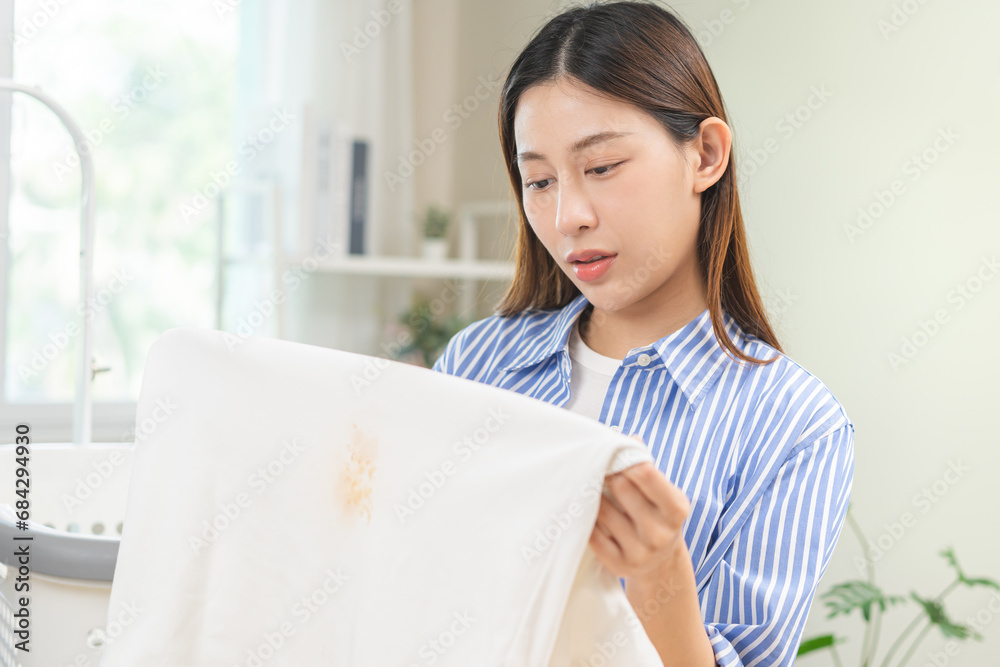 Housewife, frustrated asian young maid woman hand holding white t-shirt, showing make cloth stain, spot dirty or smudge, sauce spill, splash on clothes, dirt stains for cleaning before washing at home Housewife, frustrated asian young maid woman hand holding white t-shirt, showing make cloth stain, spot dirty or smudge, sauce spill, splash on clothes, dirt stains for cleaning before washing at home