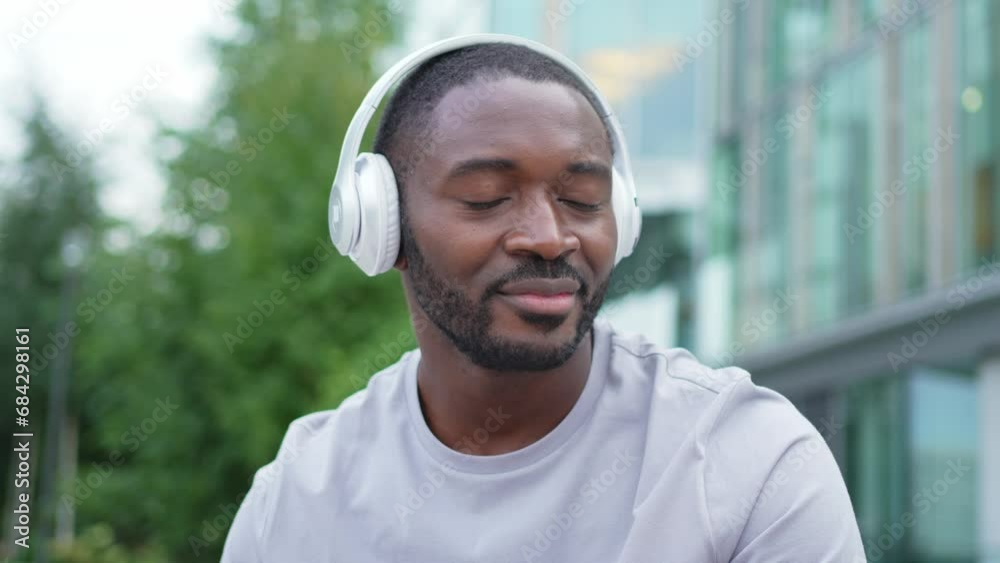 Music song concept. Good start day. Happy African American man listening modern hit on street in city. Person guy wearing headphones enjoy listening favorite music on phone. People lifestyle joy Music song concept. Good start day. Happy African American man listening modern hit on street in city. Person guy wearing headphones enjoy listening favorite music on phone. People lifestyle joy