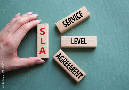 SLA - Service Level Agreement. Wooden blocks with word SLA. Businessman hand. Beautiful grey green background. Business and Service Level Agreement concept. Copy space. photo
