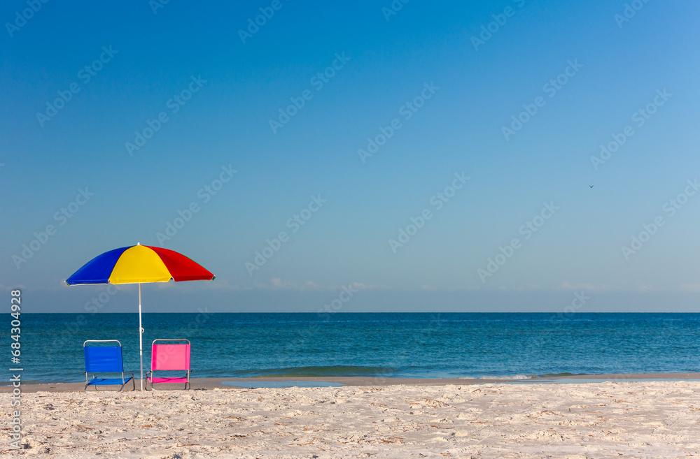 Colorful Umbrella with Pink and Blue Deckchairs on an Empty Beach