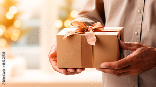 plano detalle de manos sosteniendo una caja de regalos con un fondo desenfocado, en color beige  photo