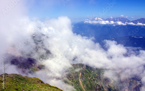 Dramatic landscape with mountain tops and white clouds against a blue sky background and space to copy