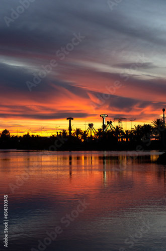 Dramatic sunset. Yellow, orange and red evening sky. Silhouettes of palm trees and park amusements