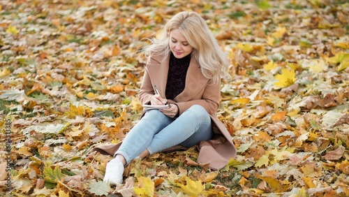 Romantic mood. Inspired woman. Diary moments. Happy lady sitting on leaves ground making notes in notebook feeling joy.