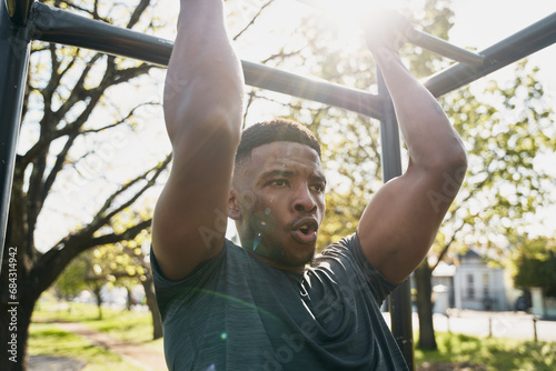 Fit young black man in t-shirt doing pull-up on monkey bars in park