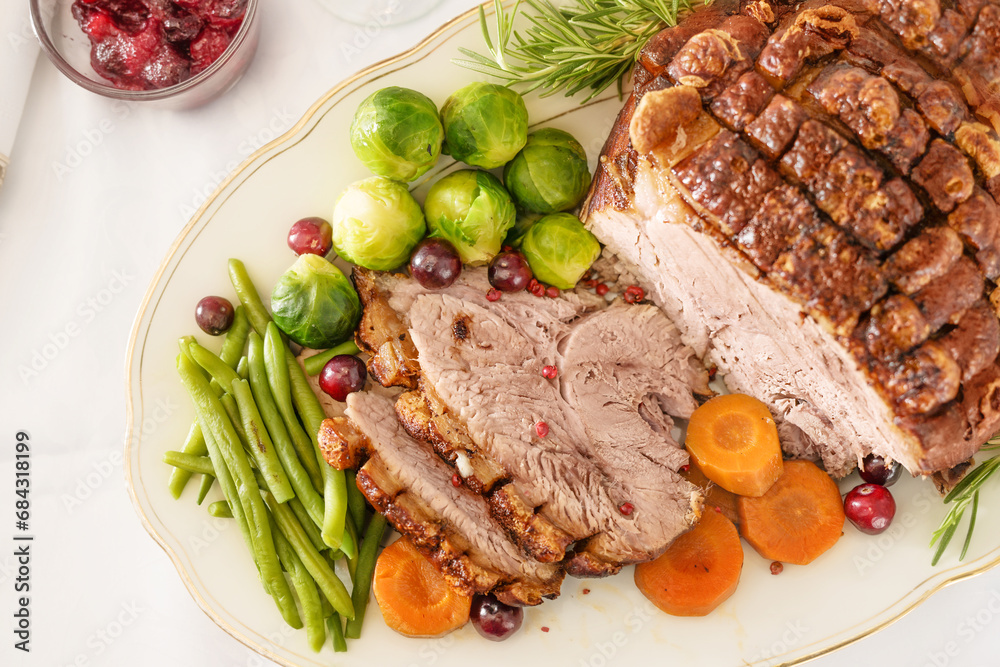 Roast pork with crust as Christmas ham with vegetables and cranberries on a white serving plate, holiday dinner, high angle view from above, copy space, selected focus Roast pork with crust as Christmas ham with vegetables and cranberries on a white serving plate, holiday dinner, high angle view from above, copy space, selected focus